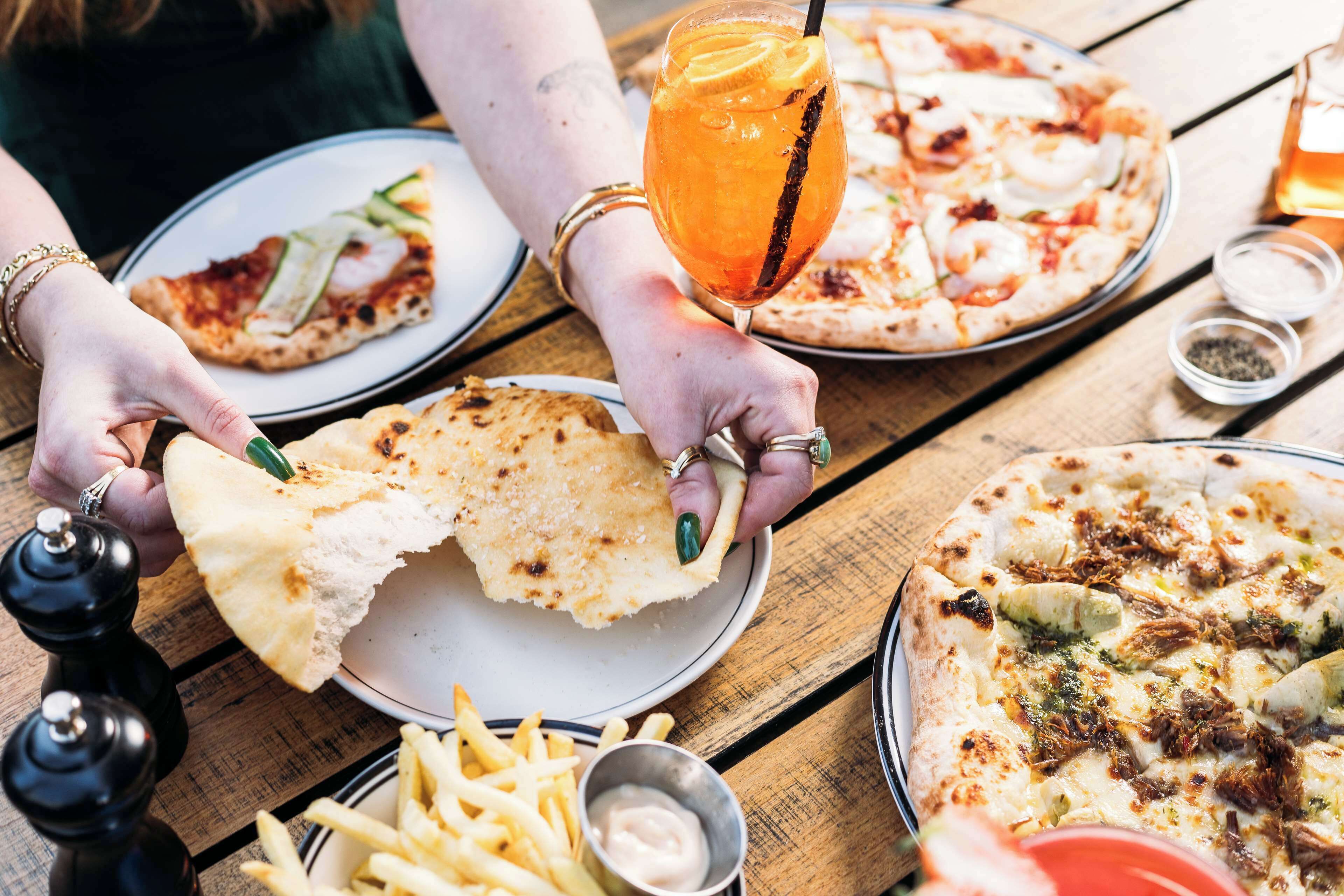 A wooden table with various food items including pizza, bread, and fries.