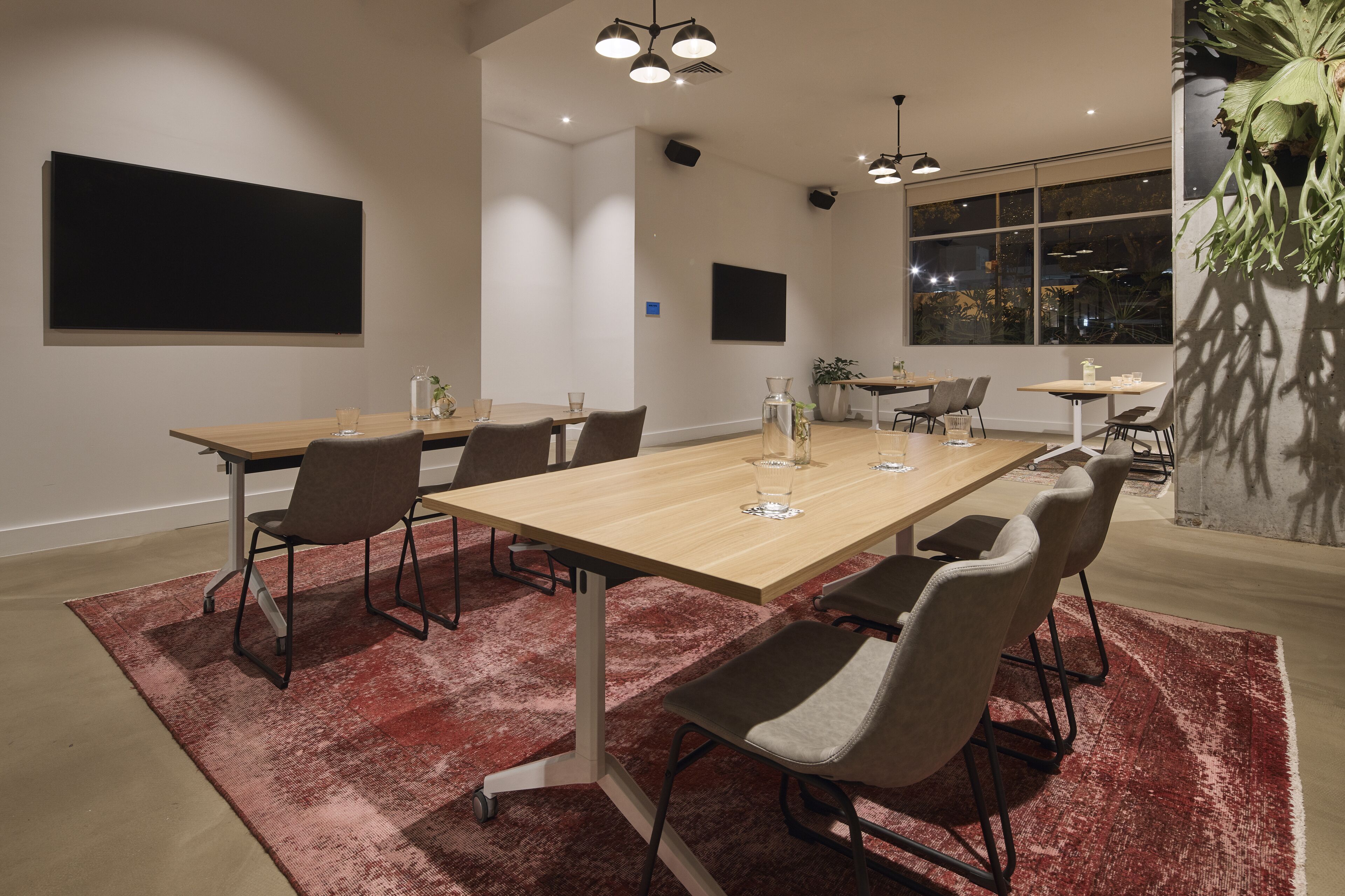 A modern conference room with a wooden table, grey chairs, and a red rug.