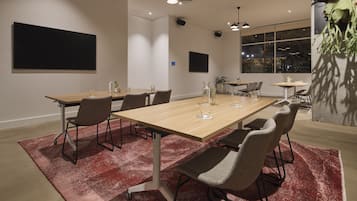 A modern conference room with a wooden table, grey chairs, and a red rug.