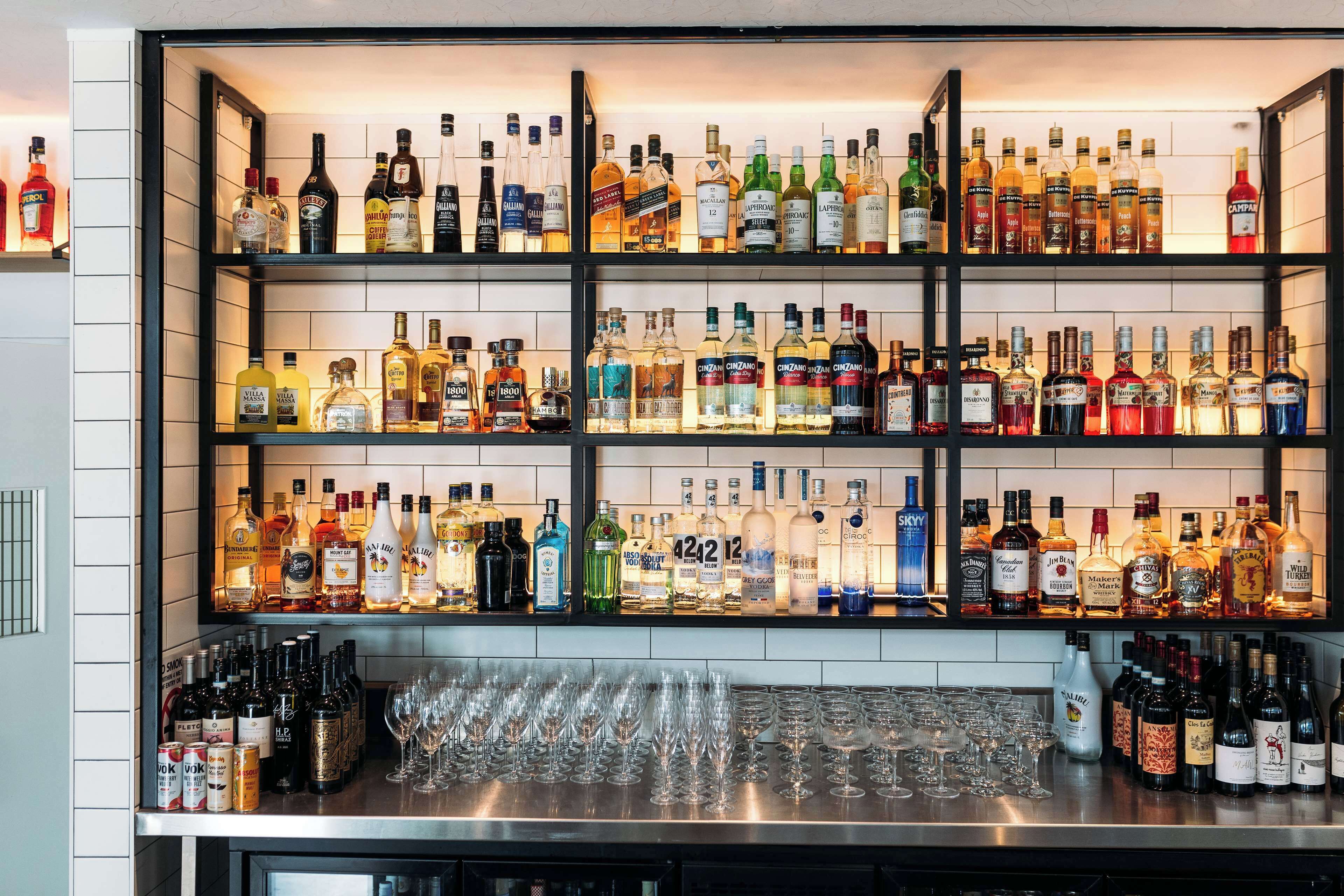 A bar with multiple shelves of liquor bottles and a variety of glasses on the counter.