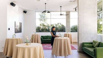 Un interior moderno con mesas redondas cubiertas con tela color beige, un sofá verde y una persona ordenando objetos en una mesa.