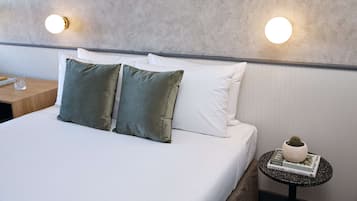 A neatly made bed with two pillows, a small round table with a book and a potted plant, and two wall-mounted lights.