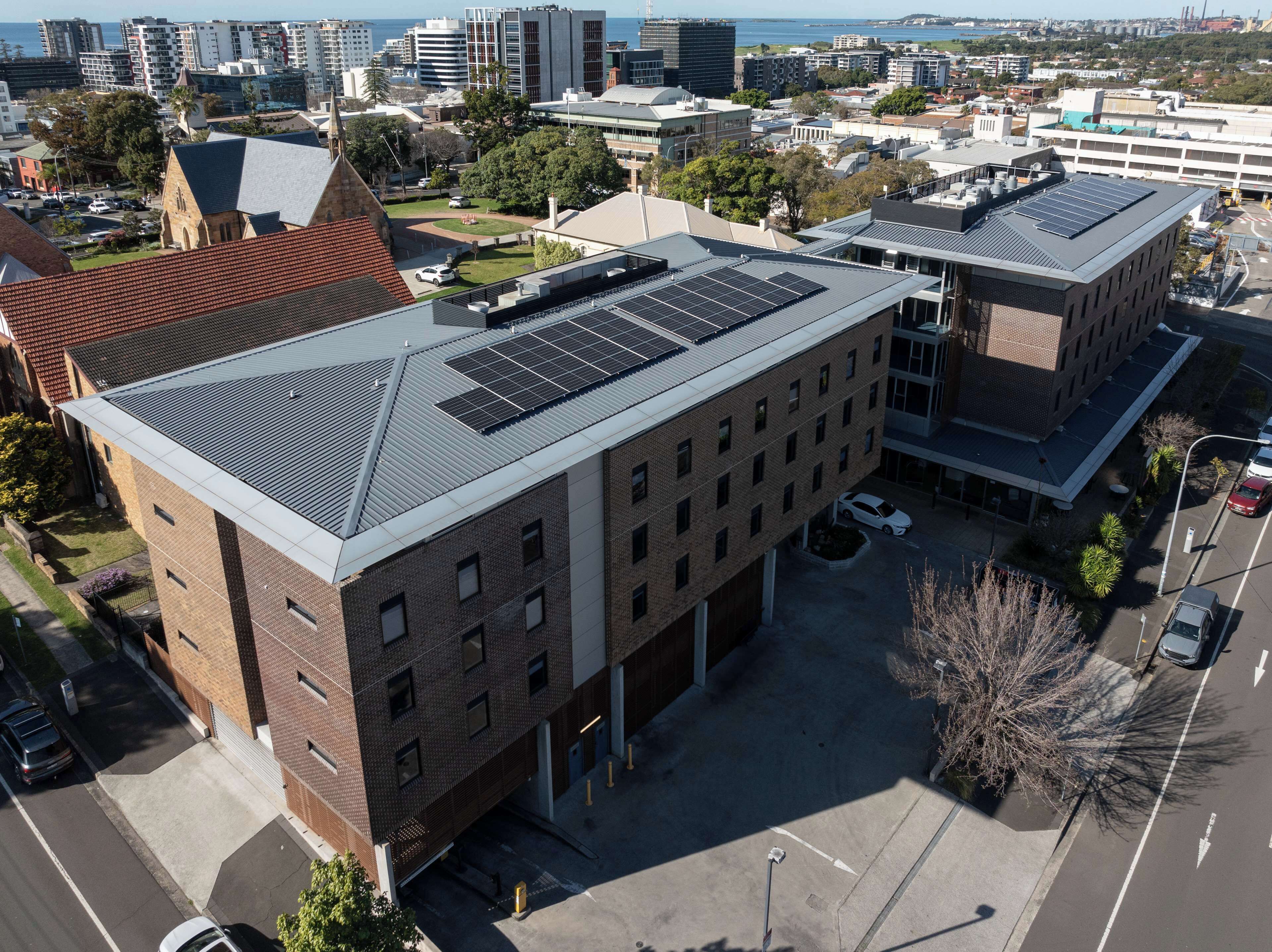 A multi-story building with a flat roof, solar panels, and a parking area.