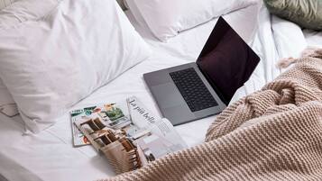 Ein Laptop auf einem Bett mit einer Zeitschrift und einer kleinen Holzschatulle.