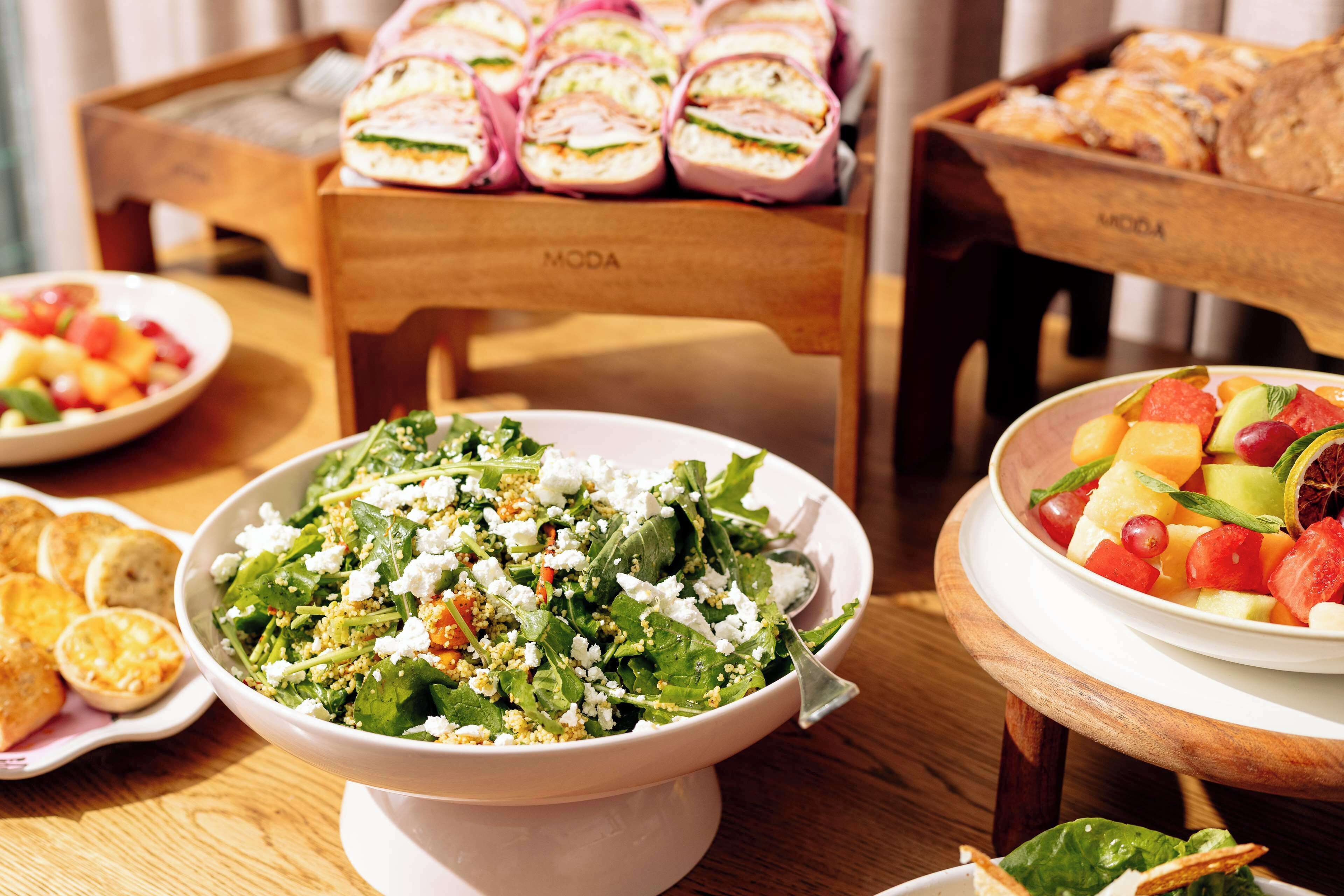 Une table de buffet proposant divers plats, notamment une salade, des fruits et des sandwichs.
