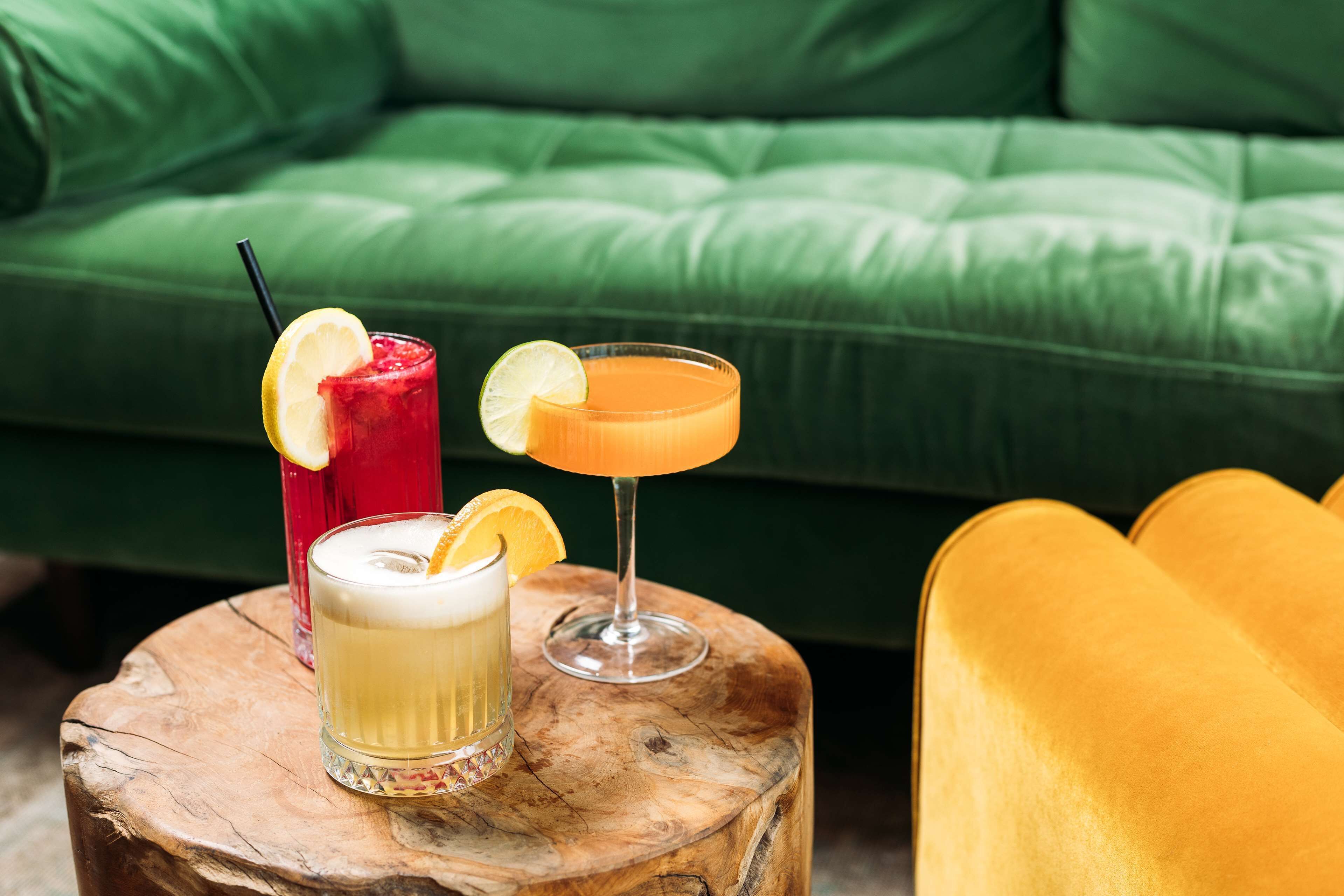 Three drinks on a wooden stool with a green couch in the background.