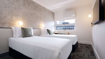 Ein Hotelzimmer mit einem großen Bett, zwei Nachttischen, einem Fenster mit Blick auf Gebäude und einer Wand-Klimaanlage.
