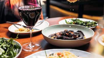 Uma mesa de jantar com vários pratos, um copo de vinho tinto e uma mão polvilhando tempero.