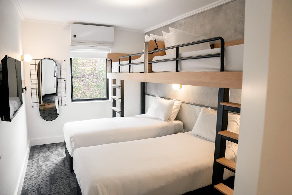 Ein Zimmer mit zwei Etagenbetten, einem kleinen Spiegel, einem Fenster mit Blick und einer Klimaanlage.