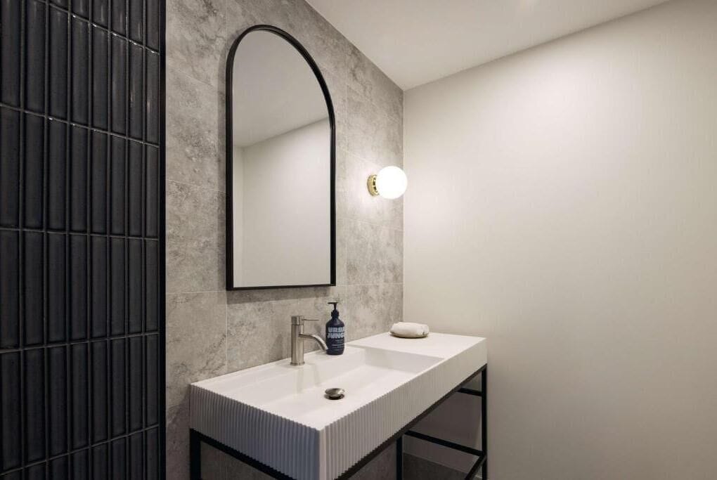 Ein modernes Badezimmer mit einem rechteckigen Waschbecken, einem großen Spiegel und einer wandmontierten Leuchte.