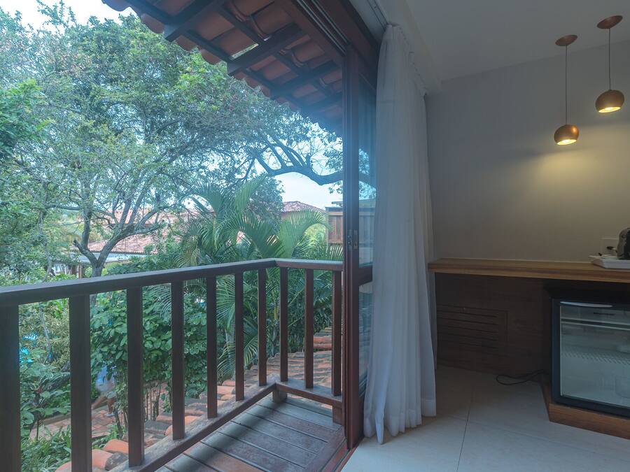 A balcony with a wooden railing, a small kitchen area with a refrigerator, and a view of lush greenery and trees.