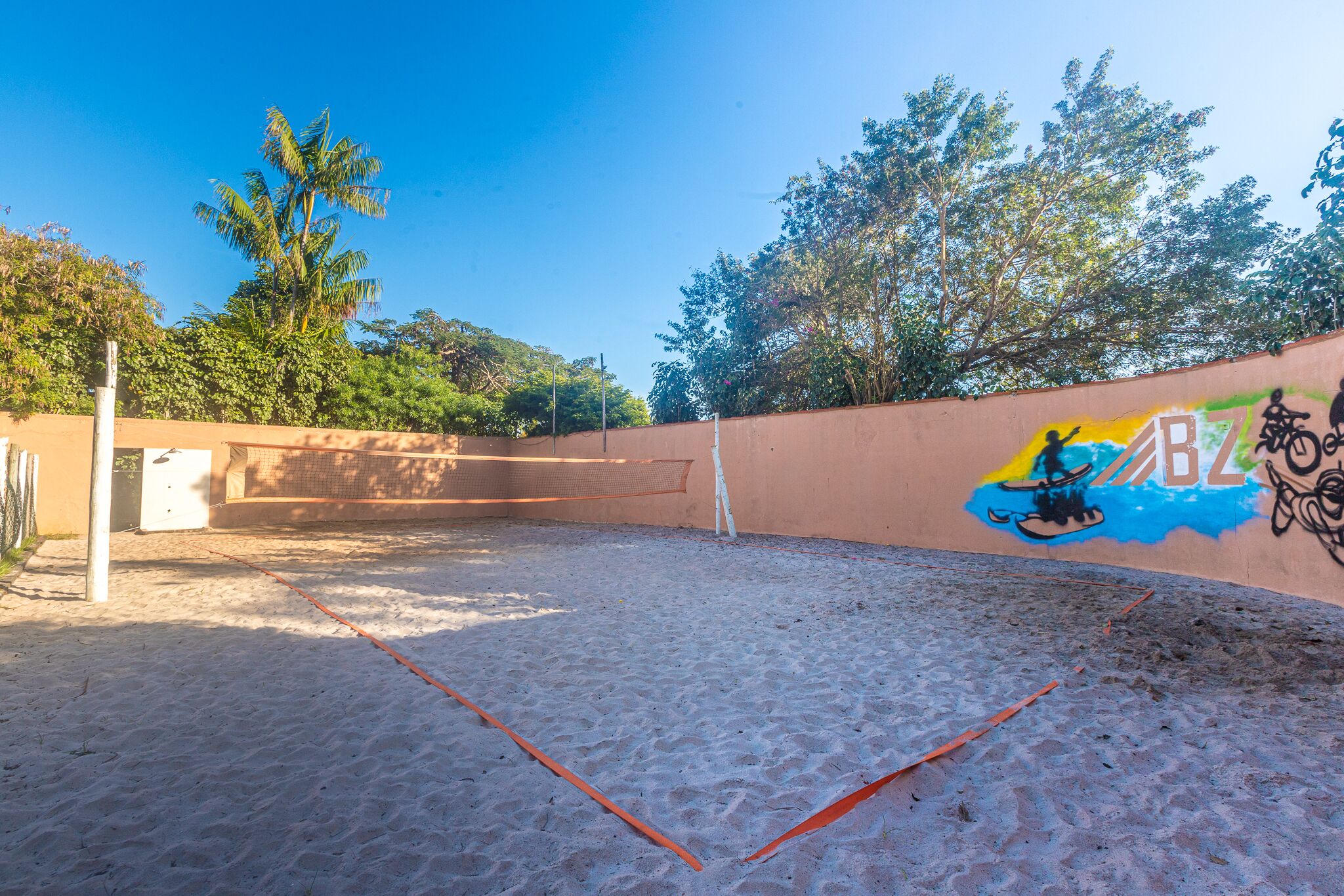 Uma quadra de tênis ao ar livre com superfície de areia, cercada por um muro baixo com pichações.