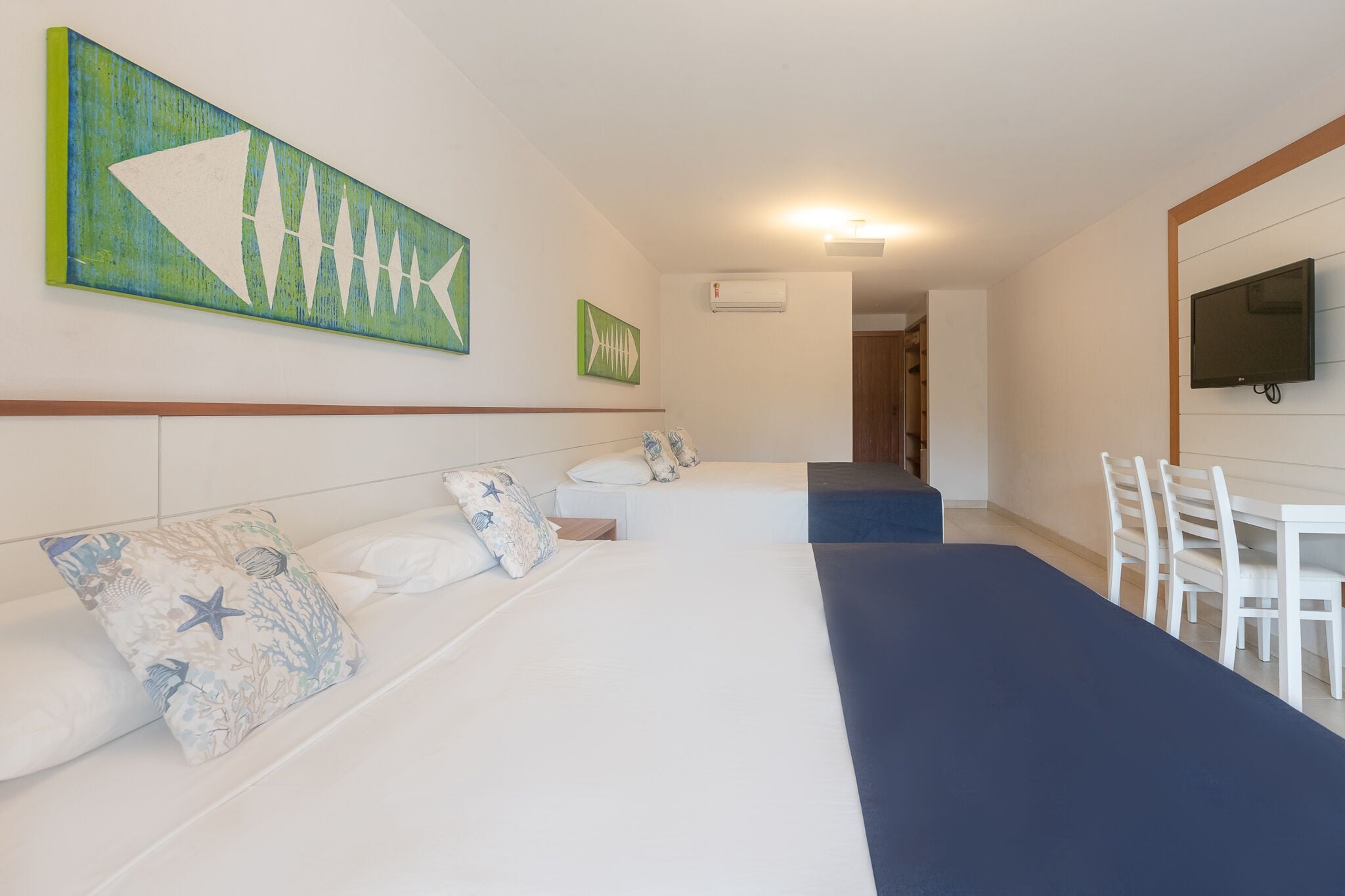 A hotel room with a large bed, a smaller bed, a desk, and a television.