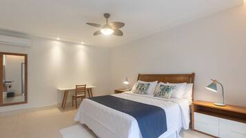 A bedroom with a bed, bedside tables, a desk, a chair, a ceiling fan, and a mirror.