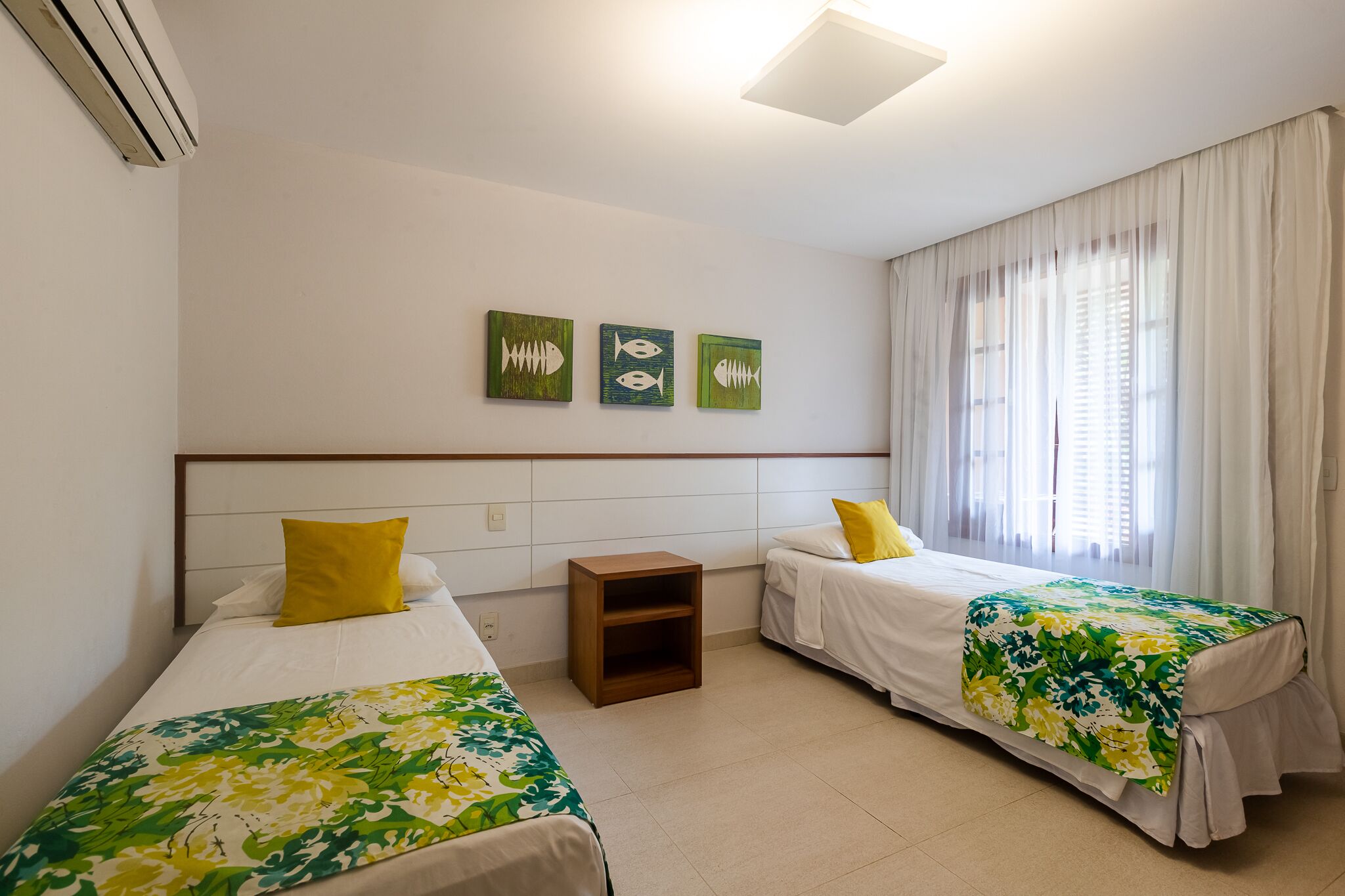 A hotel room with two single beds, a nightstand, and a large window with sheer curtains.