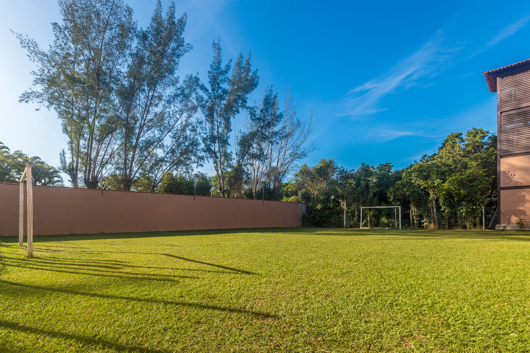 A well-maintained grassy area with a goalpost, surrounded by trees and a building with a red roof.