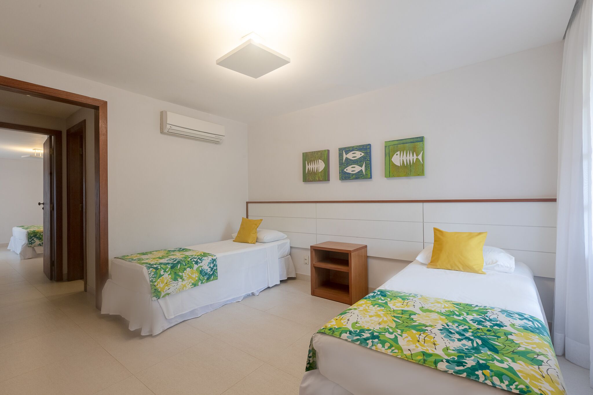 A hotel room with two single beds, a wooden nightstand, and a wall-mounted air conditioner.