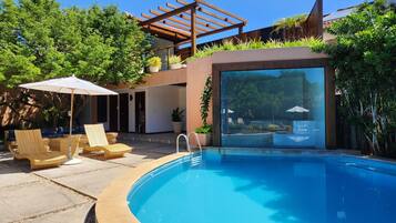 A modern outdoor pool area with a pergola, lounge chairs, and a view of the pool through a glass wall.