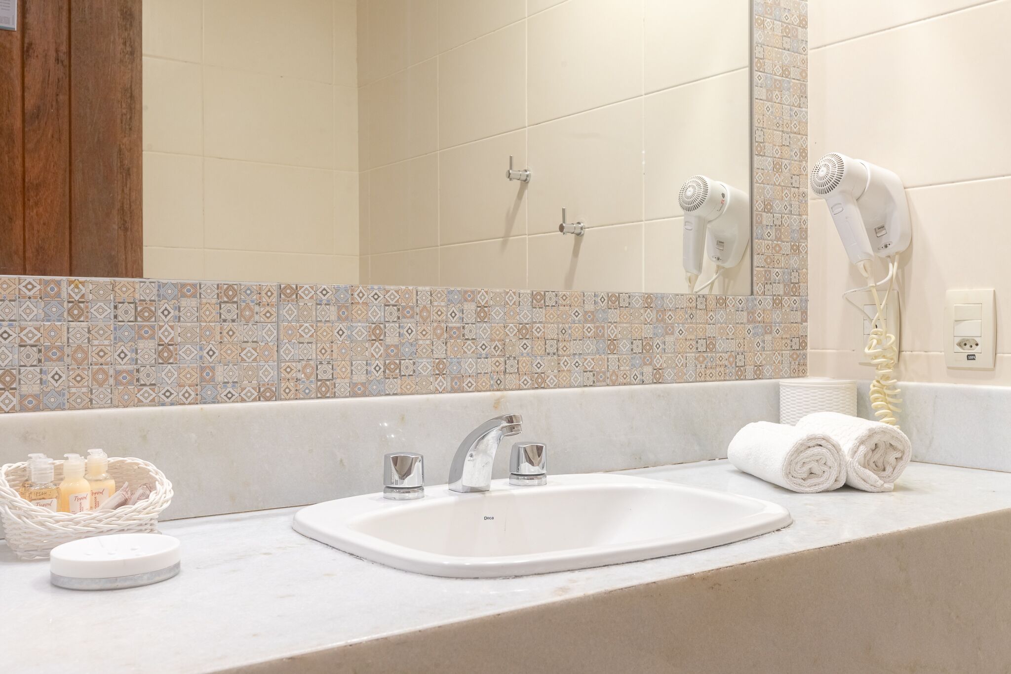 A bathroom with a white sink, two faucets, a mirror, and a hairdryer on the wall.