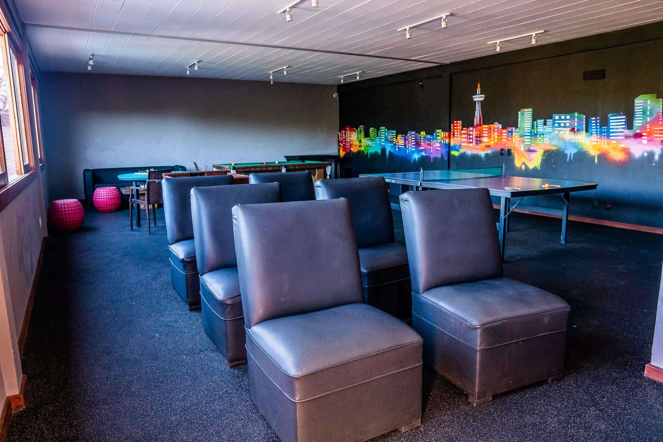 Un'area lounge moderna con sedute in pelle, un tavolo da biliardo e un murale raffigurante un panorama cittadino.