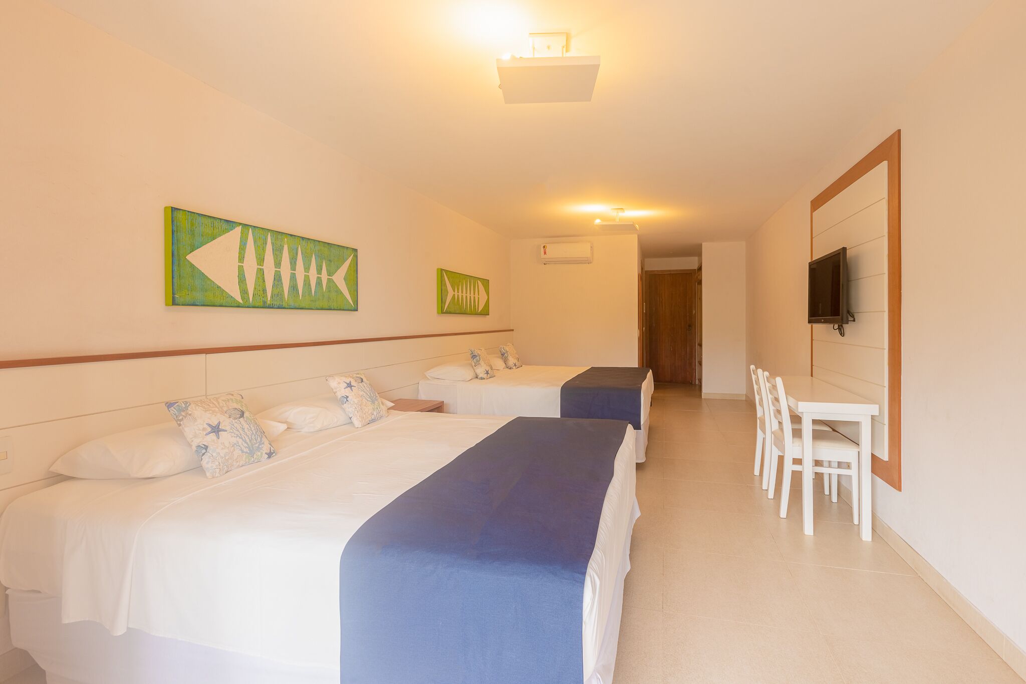 A hotel room with two beds, a dining table with chairs, and a TV mounted on the wall.