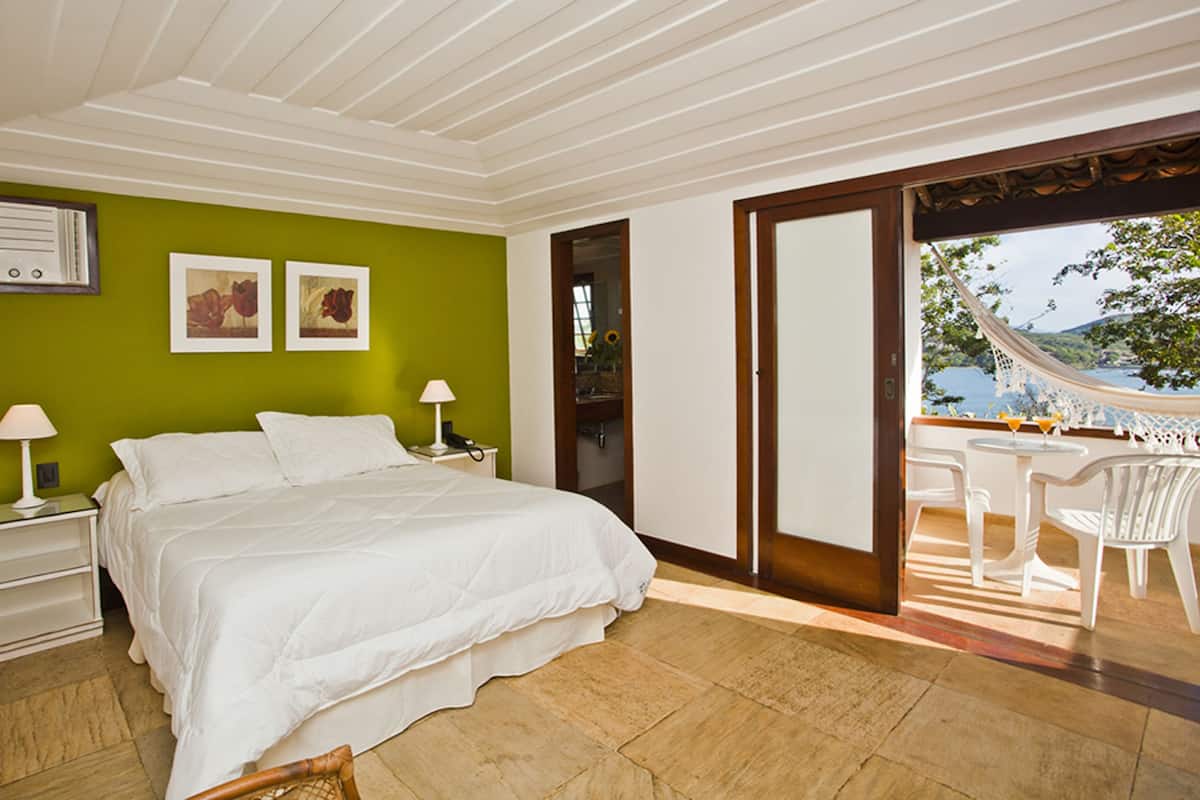 A bedroom with a bed, bedside tables, a nightstand, a green wall, and a view of the outdoors.