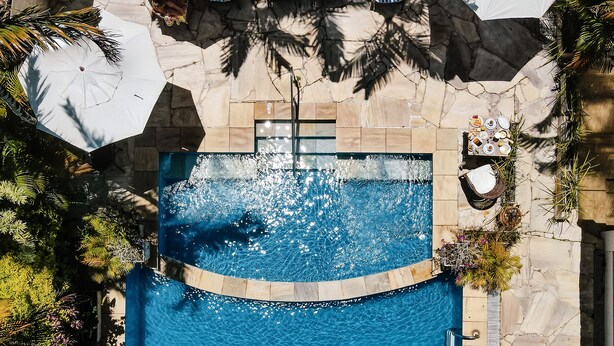A top-down view of a swimming pool with a stone deck, surrounded by lounge chairs and umbrellas, and various plants. - Auberge de La Langouste (Búzios)