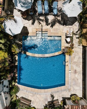 A top-down view of a swimming pool with a stone deck, surrounded by lounge chairs and umbrellas, and various plants. - Auberge de La Langouste (Búzios)