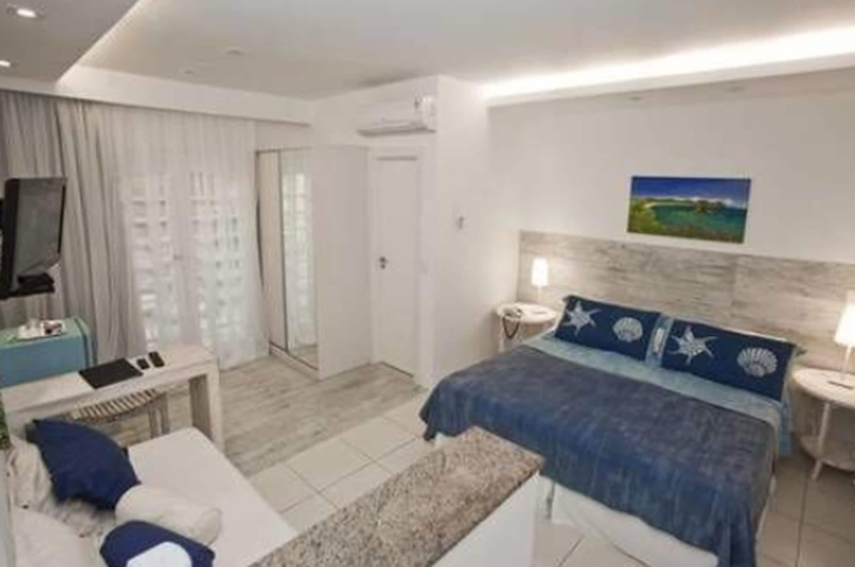 Quarto de hotel moderno com cama, mesas de cabeceira, escrivaninha e televisão.