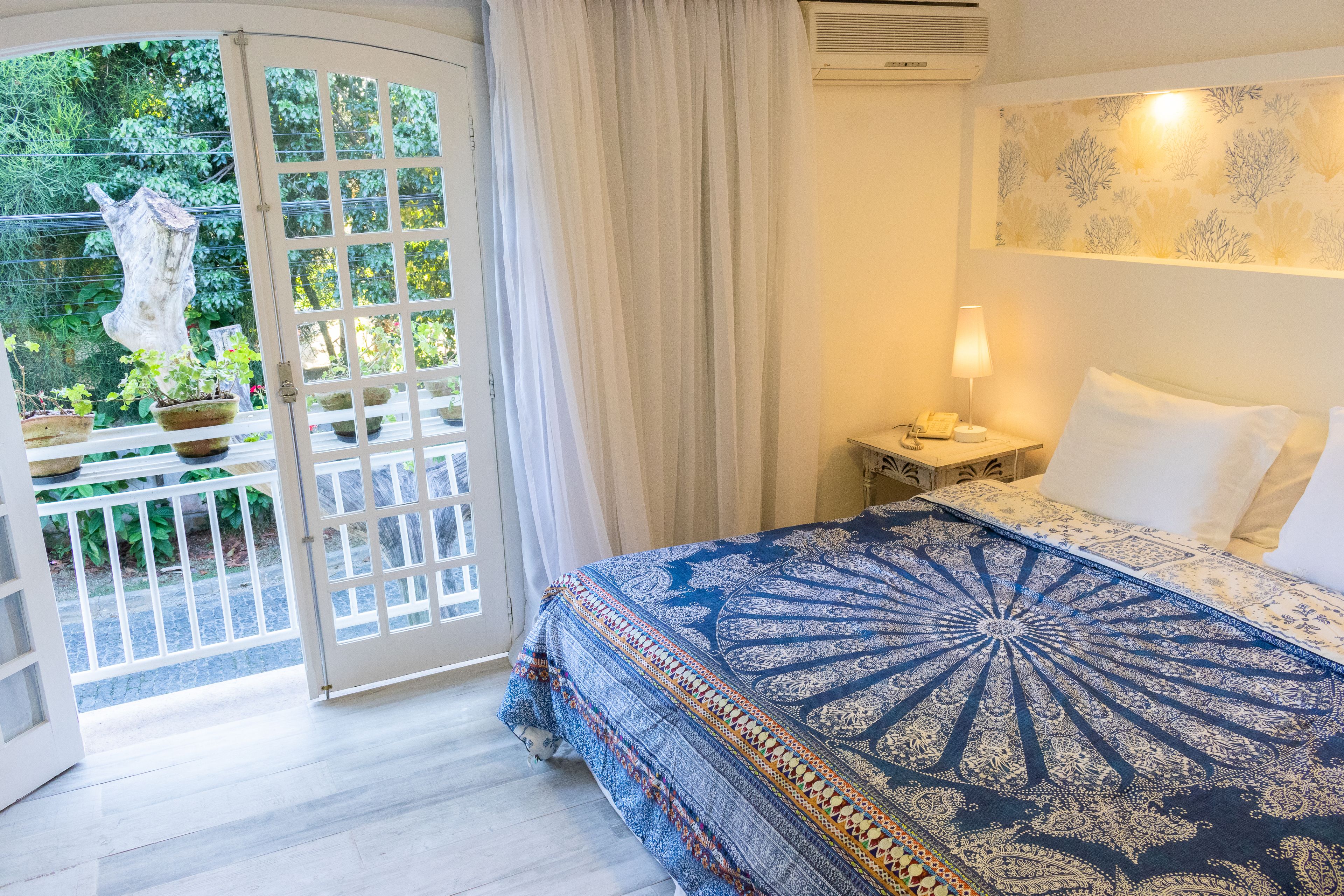 A bedroom with a large bed, a nightstand, a lamp, and a view of a garden through a glass door.