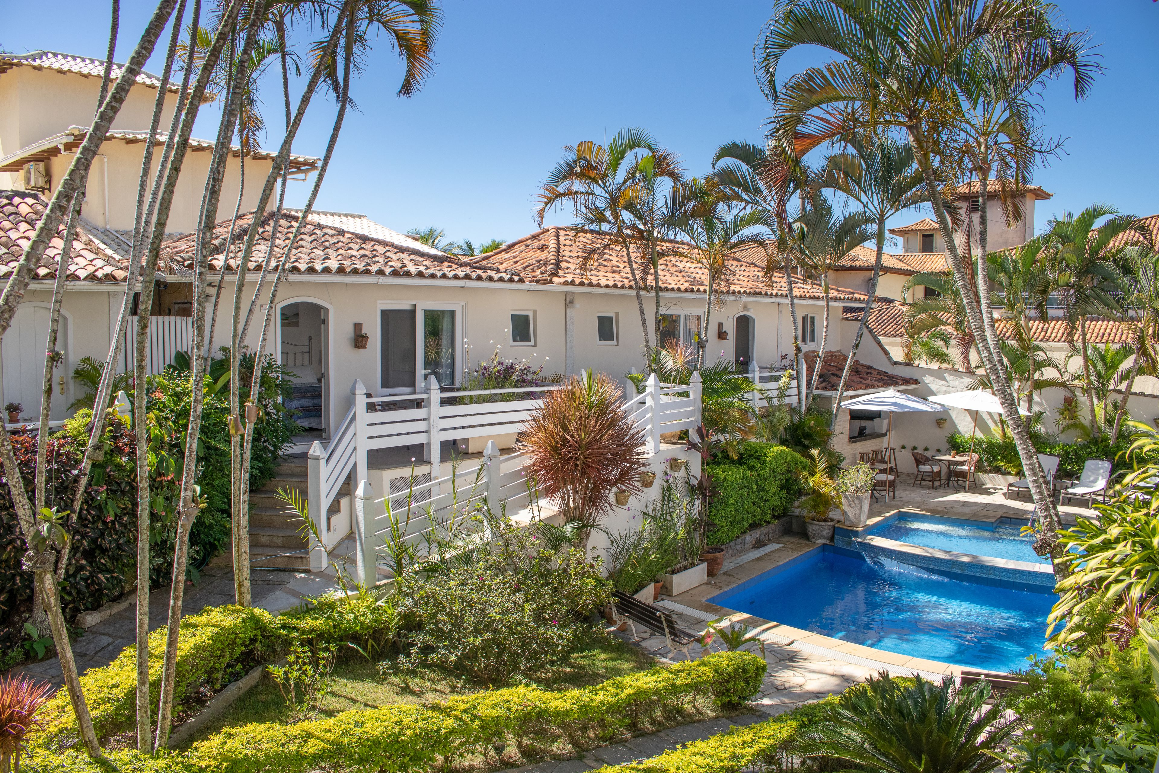 A resort with a swimming pool, palm trees, and a white fence.