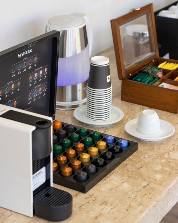 A coffee machine with a menu display, a stack of disposable cups, a coffee pot, and a drawer with utensils. - Auberge de La Langouste (Búzios)
