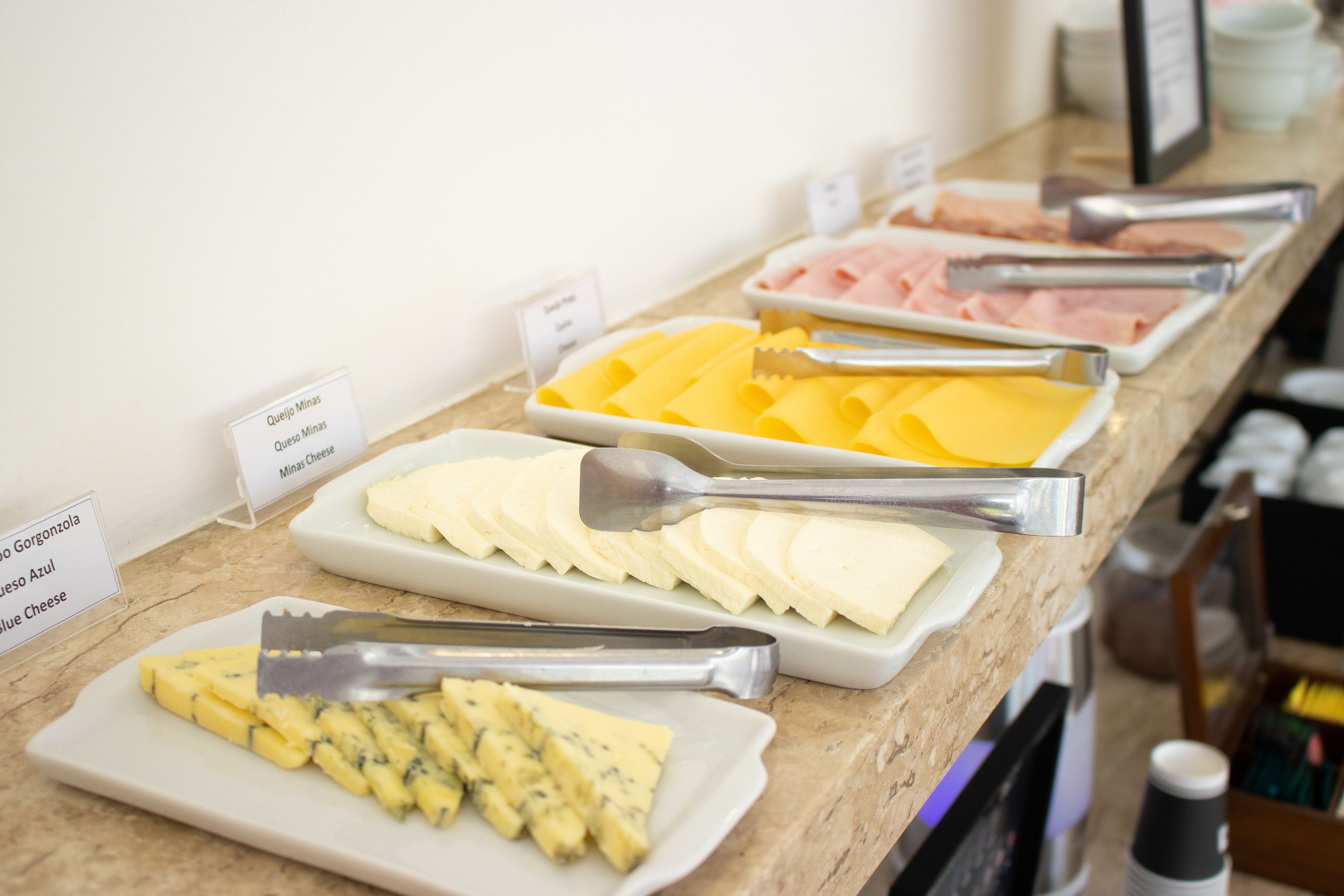 A buffet with various cheese and meat options, including queso minas and queso azul, arranged on a marble counter.