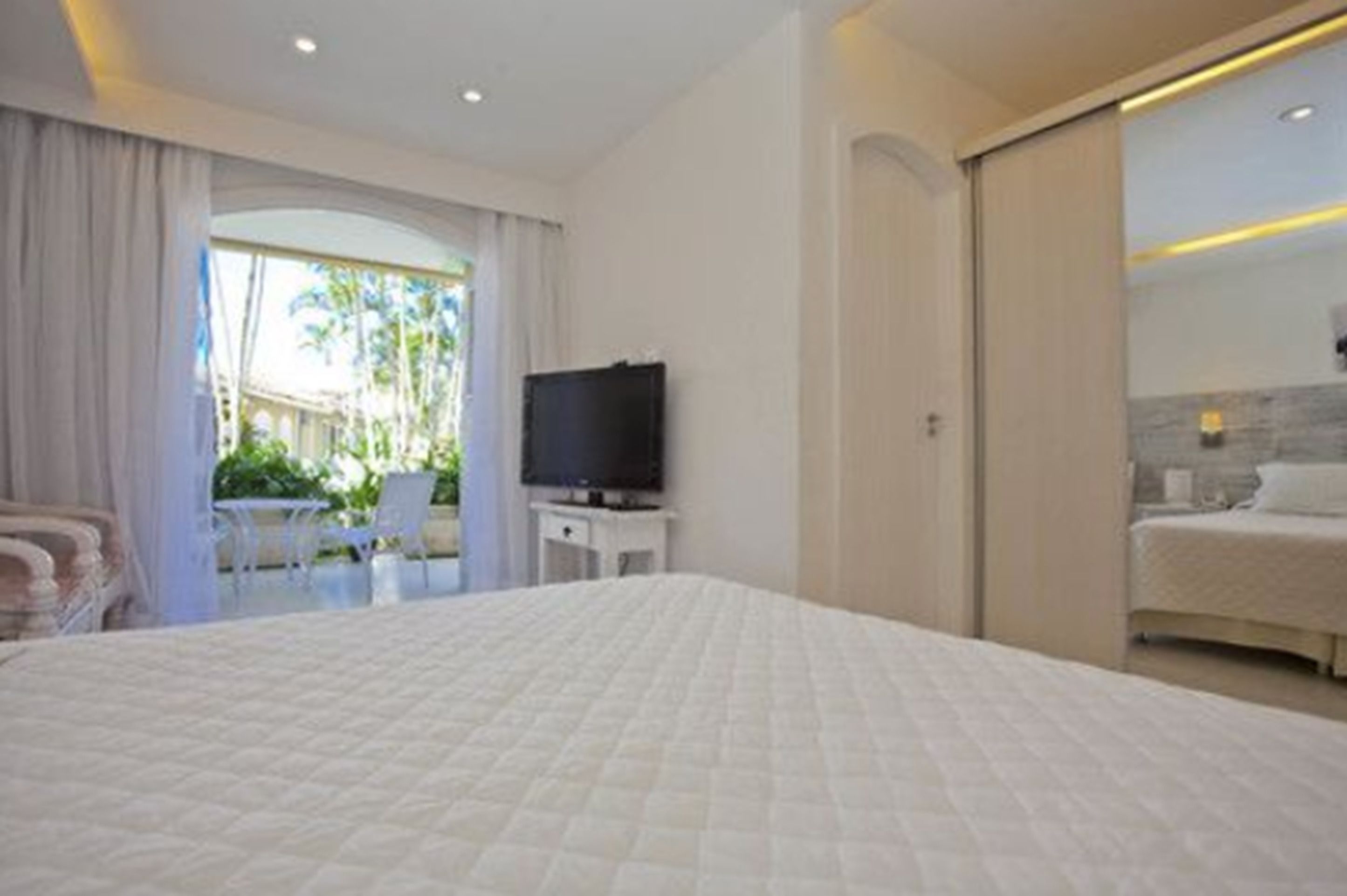 A hotel room with a large bed, a television, and a sliding door leading to a balcony.