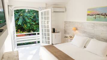 Une chambre d’hôtel avec un lit, un bureau, une lampe et une vue sur un jardin, visible par une porte ouverte.