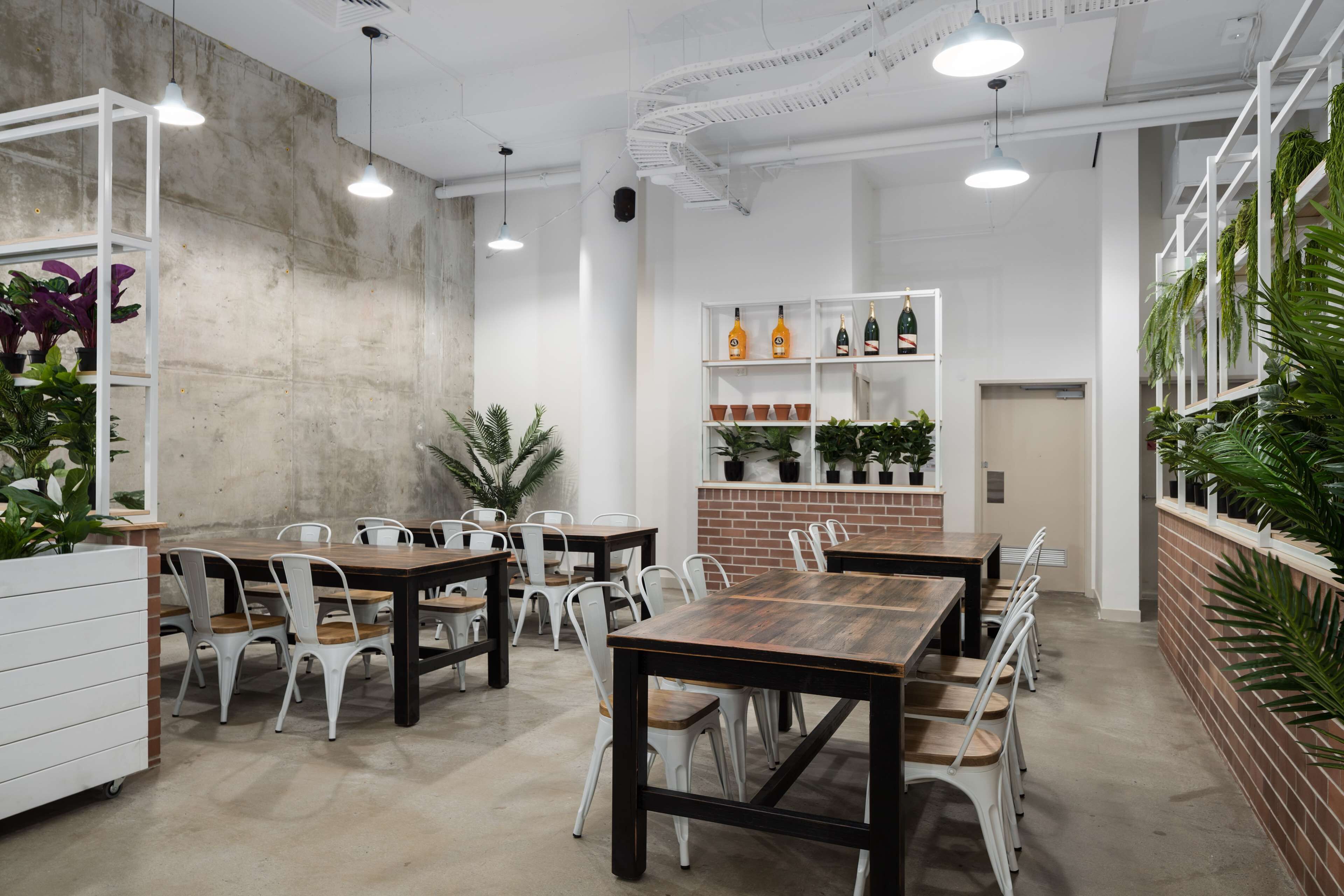 A modern dining area with wooden tables and white chairs, potted plants, and shelves with bottles.