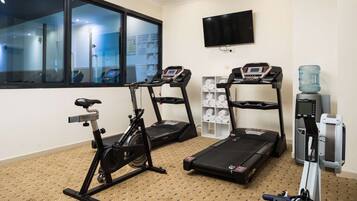 A fitness room with an exercise bike, two treadmills, and a water dispenser.