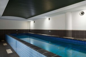 Una piscina con azulejos azules, techo oscuro y paredes blancas.