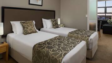 A hotel room with two beds, a nightstand, a desk, and a view of the outside.