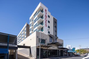 Un hotel de varios pisos con un llamativo letrero 'RYDGES', con balcones y una zona de entrada techada.