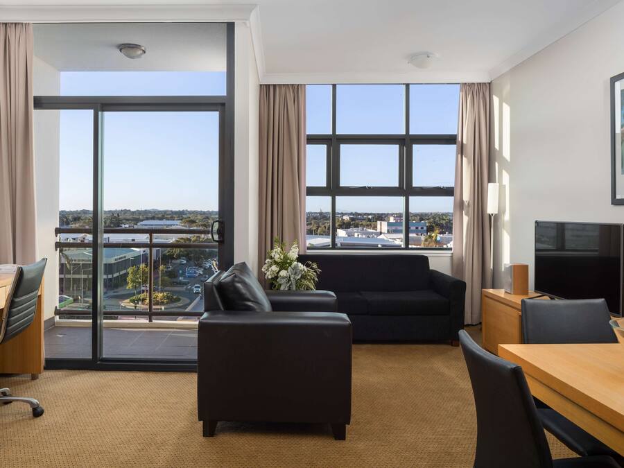 Habitación de hotel con un ventanal grande, un sofá, una mesa de comedor y un televisor.