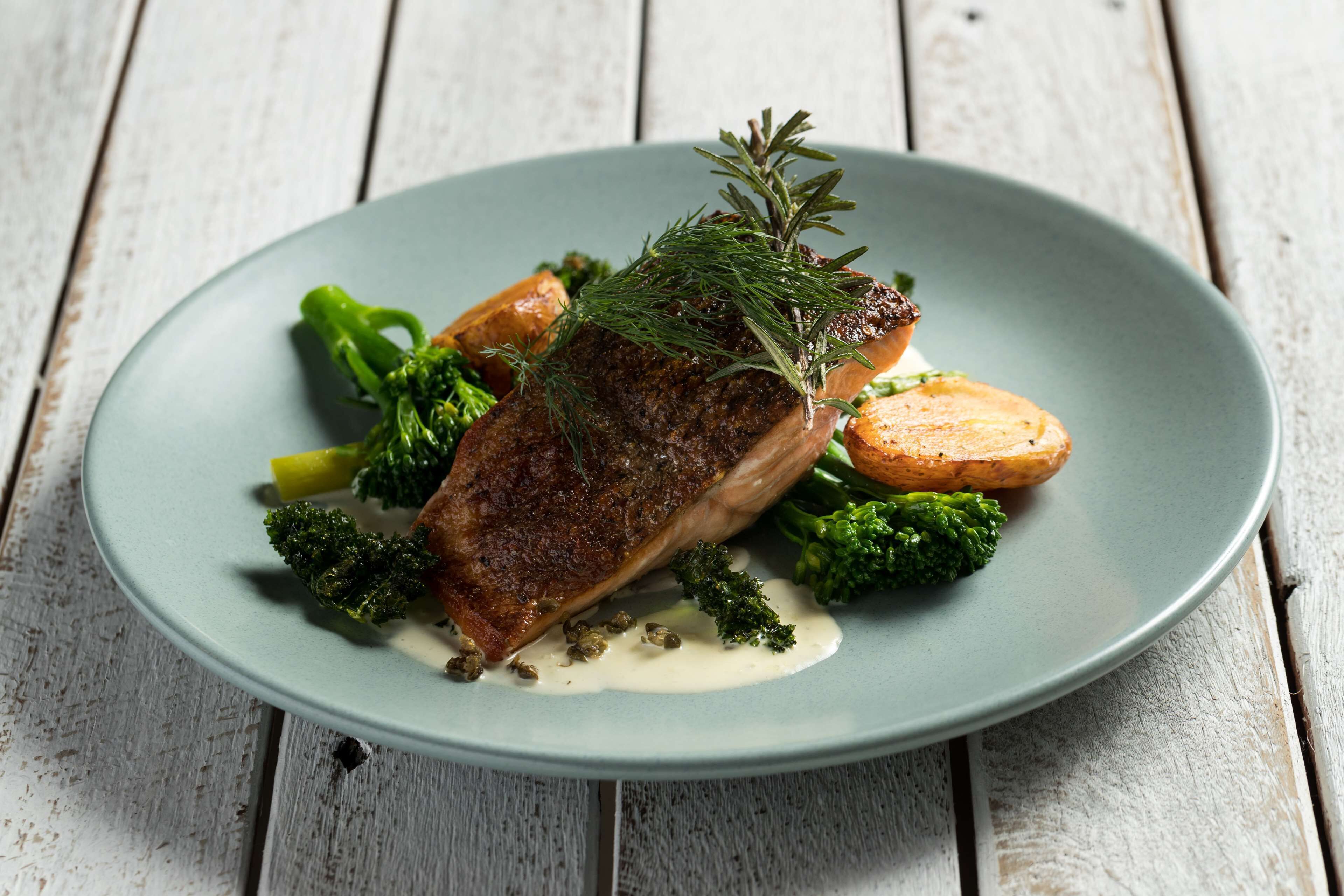 A plate with a piece of meat, broccoli, and potatoes on a rustic wooden table.