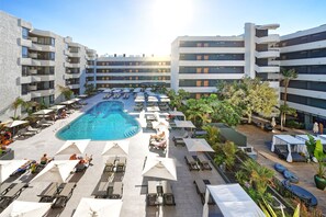 Un hotel con piscina central rodeada de tumbonas y sombrillas, varios pisos y un diseño arquitectónico moderno.