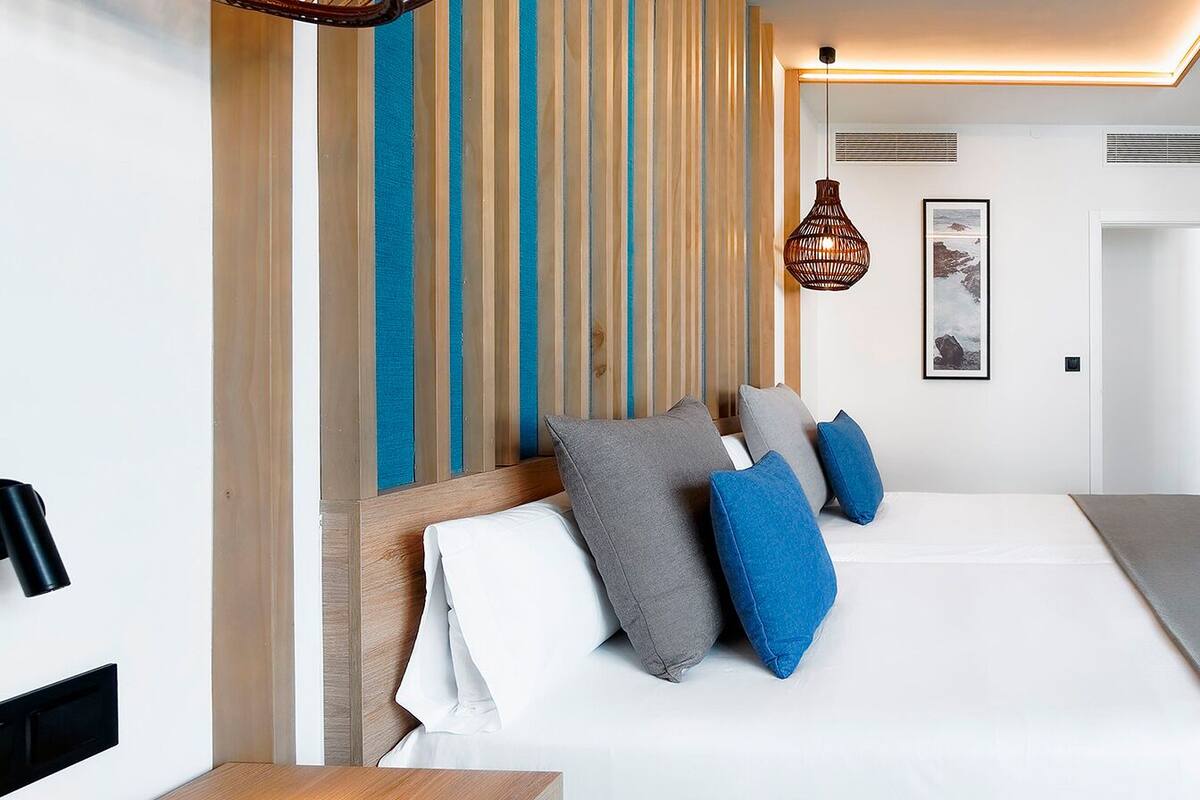 A modern hotel room with a large bed, a TV, and a wooden headboard.