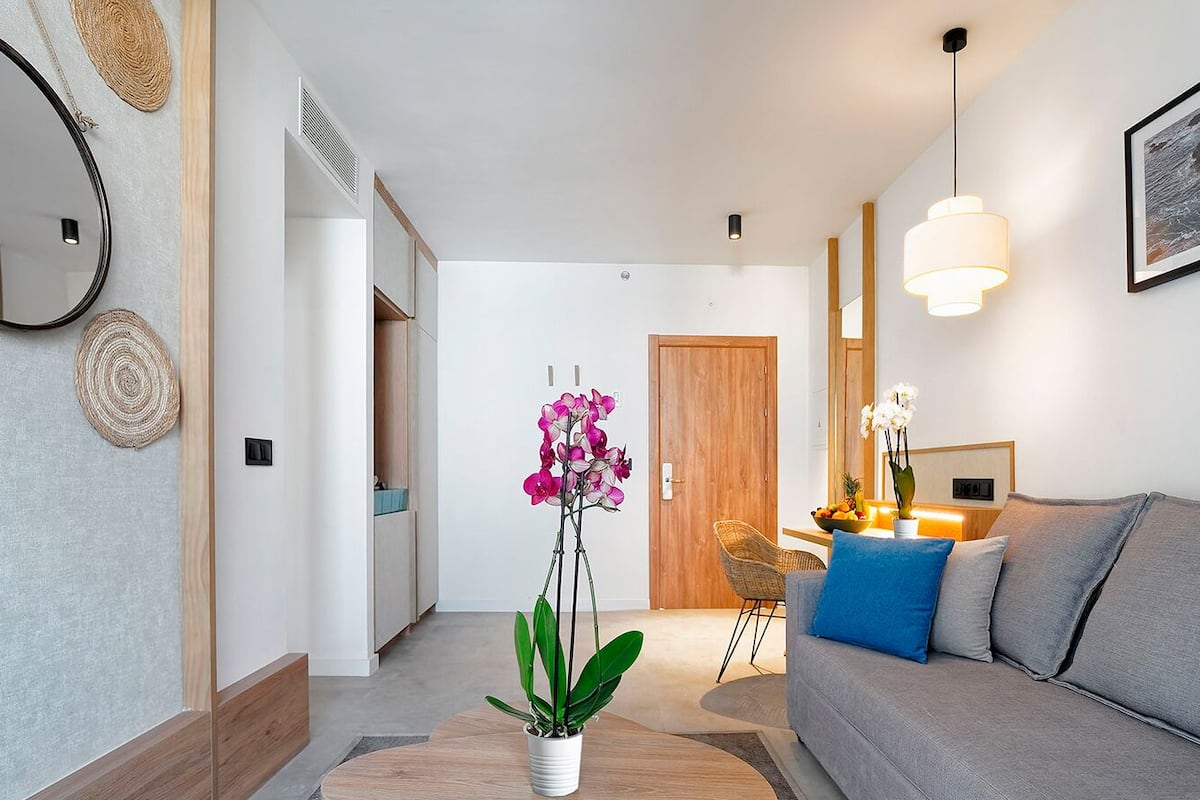 A modern living room with a grey sofa, a coffee table with a potted orchid, and a dining area with a table set for two.