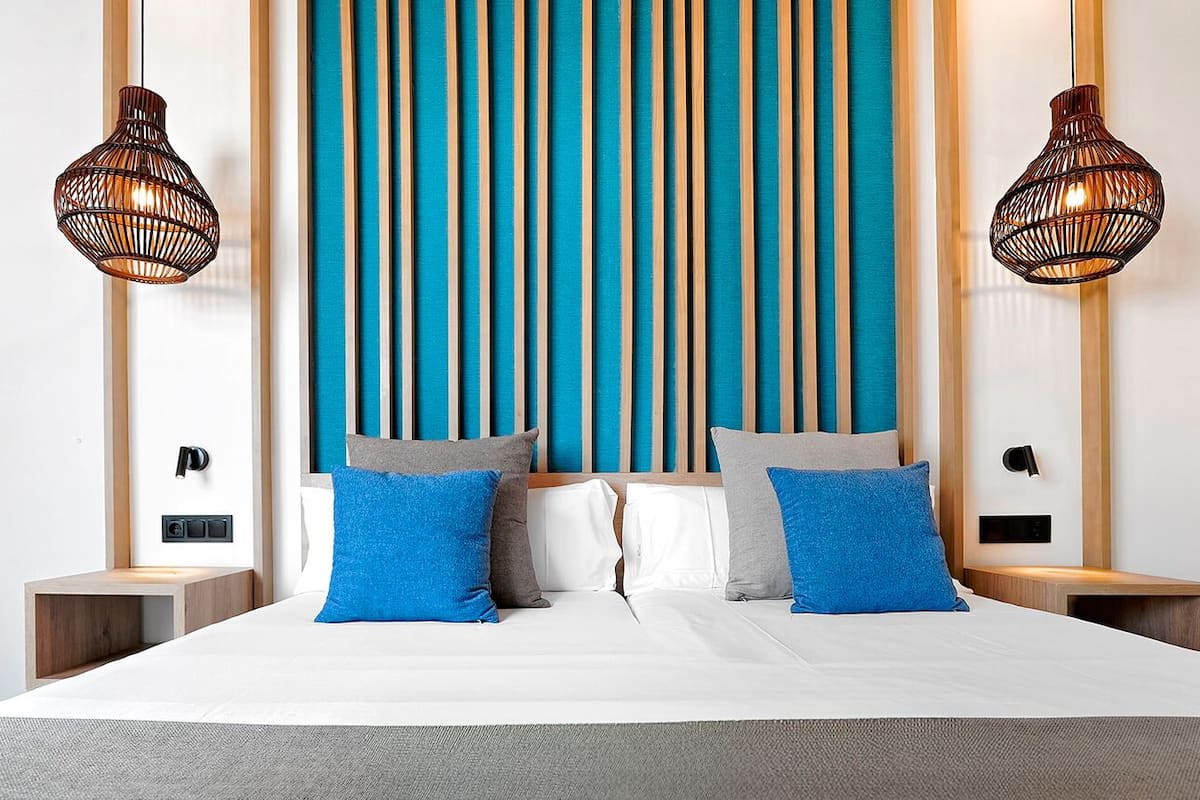 A modern hotel room with a large bed, two bedside tables, a wall-mounted TV, and a vertical striped wall design.