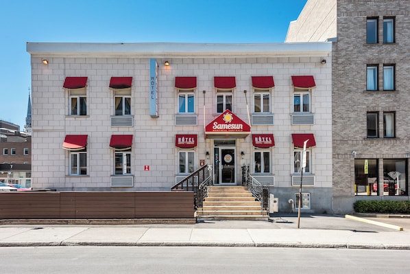 Un hôtel avec un auvent rouge, une enseigne indiquant « Samesun Montreal Central » et un escalier menant à l’entrée.