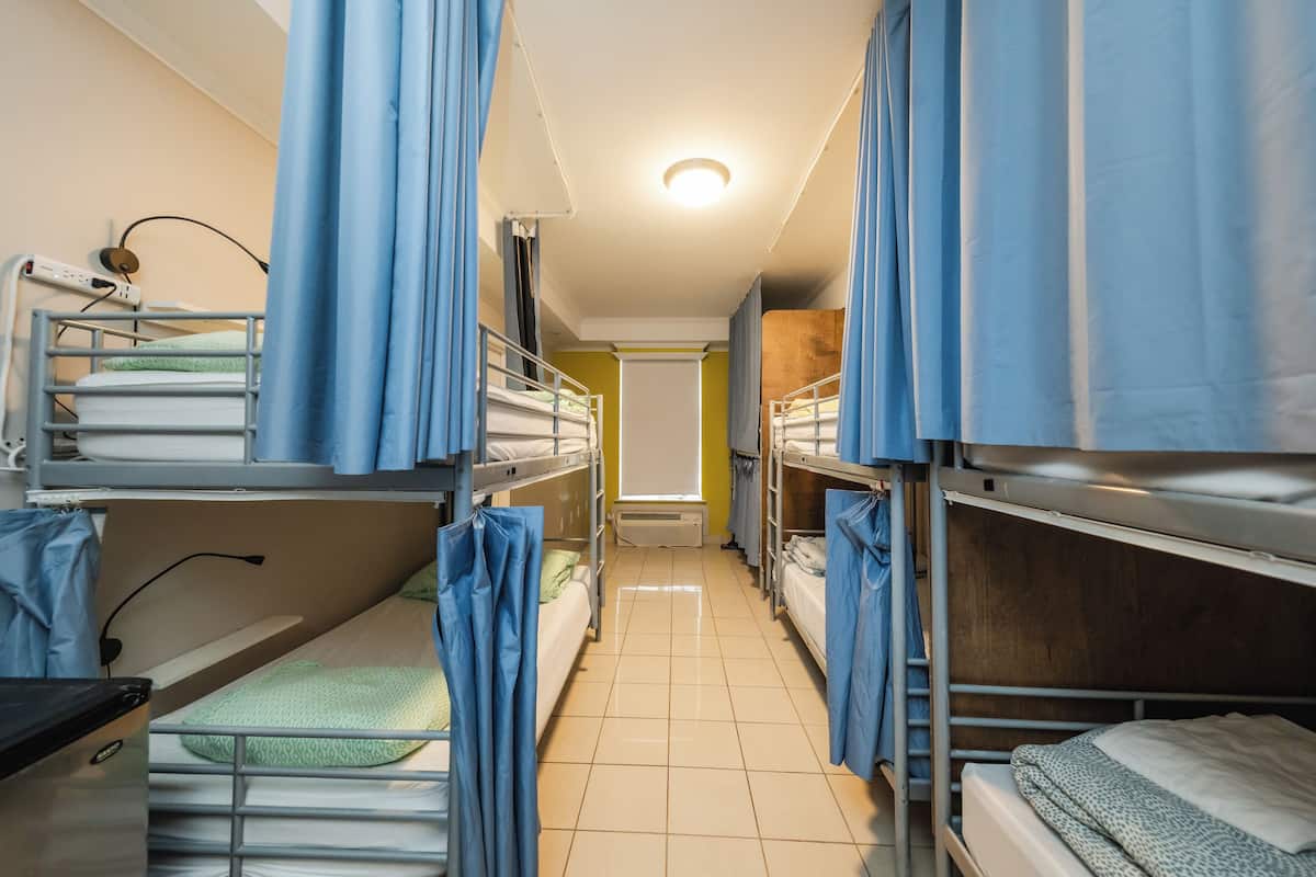 Um corredor estreito com beliches em ambos os lados, um quadro branco na parede e uma lâmpada no teto.