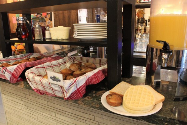 Un bufé de desayuno con pan, muffins y jugo.