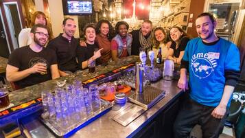 Un groupe de personnes est réuni dans un bar, avec un comptoir, des verres et un téléviseur en arrière-plan.